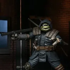 The Last Ronin action figure in a gray cloak and hood, wielding a chained kusarigama against a dark brick background