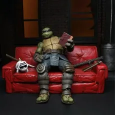 The Last Ronin action figure sitting on a red couch, reading a book next to his pet robotic cat and weapons