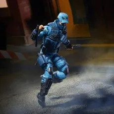 G.I. Joe Shockwave figure in blue camo crouching behind a red brick corner, aiming a pistol at an enemy in the shadow..