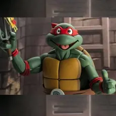 Close-up of TMNT Raphael toy with red mask, smiling, and giving a thumbs up against a brick wall.
