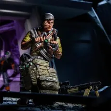 G.I. Joe Tunnel Rat figure kneeling, adjusting his gear near a mounted machine gun and large backpack.