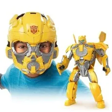 Child wearing a large Bumblebee helmet next to the matching yellow and silver Transformers robot action figure.