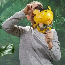 Boy holding up a yellow plastic Bumblebee mask from Transformers against a jungle background.