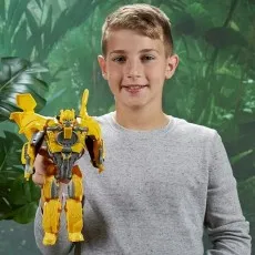 Smiling boy in a gray shirt holding up a fully transformed yellow Bumblebee robot action figure.