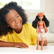 A smiling girl with curly hair looks at her Disney Princess Moana doll.