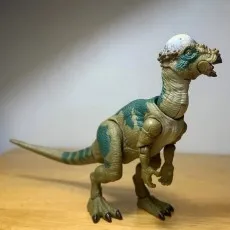 Pachycephalosaurus action figure standing on a wooden surface, viewed from a three-quarter angle.