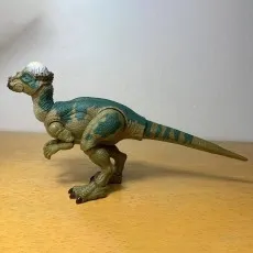 Side profile of the Pachycephalosaurus action figure with green and tan markings on a wooden surface.