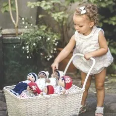 Toddler pushing a white wicker cart full of various baby dolls outside.