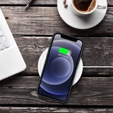 iPhone 12 in a black silicone case charging on a wireless pad next to a coffee cup.