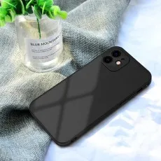 Sleek black silicone iPhone 12 case lying on a grey fabric next to a small green plant.